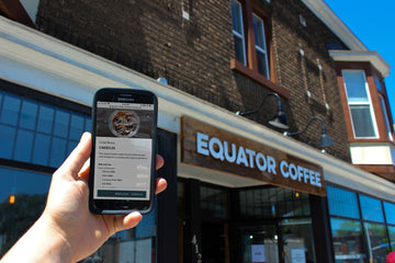 A person holding a phone with the Equator App showing, and they are in front one of our cafes.