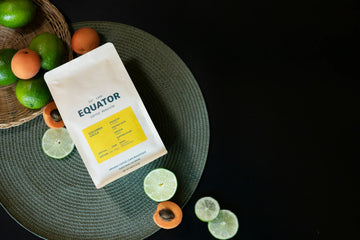 Bag of Colombia Single Origin coffee with limes and apricots on a green mat with a black background.