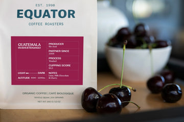 340g bag of Guatemala single origin coffee on counter with cherries in front of it and a bowl of cherries beside it.