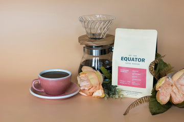 Cup of coffee with a Hario V60 in the background and a bag of Honduras Marcala coffee.
