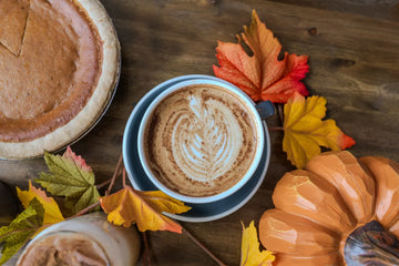 Pumpkin Spiced Latte surrounded by leaves, a pumpkin and pumpkin pie.